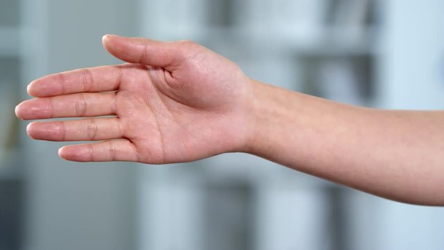 Close-upshot of unrecognizable woman raising bare hand with palm facing towards camera and holding it horizontally, on blurred background. Video suitable for adding AR, VR graphics and elements.