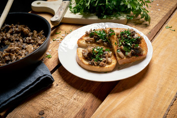 Toasts with mushrooms on white plate on wooden kitchen table
