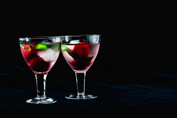 cocktail with ice mint strawberries cherries kiwi in glasses on a black background one