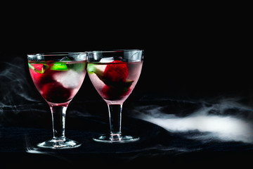 Cocktail with ice mint strawberries cherries kiwi in glasses on a black background in smoke two