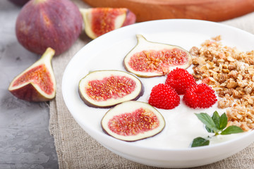 Yoghurt with raspberry, granola and figs in white plate on a gray concrete background and linen textile. side view, selective focus.
