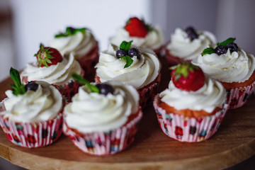 Tasty muffins decorated with red and blue berries and mint leaf.
