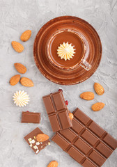Cup of hot chocolate and pieces of milk chocolate with almonds on a gray concrete background. Top view.
