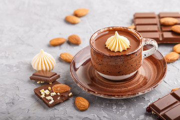Cup of hot chocolate and pieces of milk chocolate with almonds on a gray concrete background. Side view, selective focus.