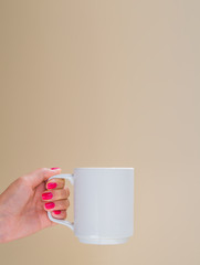 Mockup woman with red manicure holds white ceramic cup isolated on beige. Copy space for your text