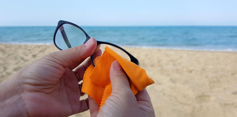 Donna che pulisce occhiali da vista sulla spiaggia