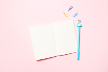 Notepad with colored pen and paper clips on a pink background. School and workspace concept. Flat lay, top view