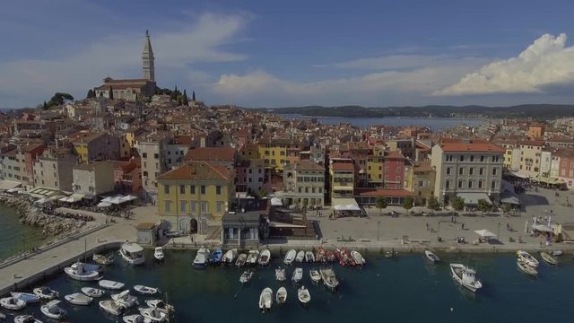 Stabile aerial drone video of Rovini old town with church and tower. Birds flying around on a bright sunny day over the harbour.