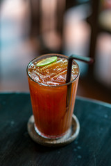 Vertical shot of cold tea in a glass with a straw on wooden table in a coffee shop. Selective focus. Perfect ice-cold drink for a hot summer day.