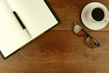 From above of notebook and pen on wooden table with cup of espresso and eyeglasses in modern workplace
