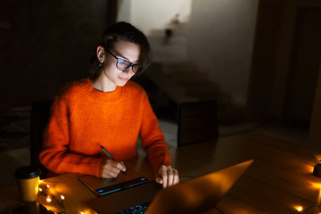 Portrait of smiling designer girl, working at graphic tablet on laptop. Wearing eyeglasses and...