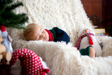 Baby boy, cute child, wearing santa claus robe sitting in rocking chair with Christmas tree and lights on