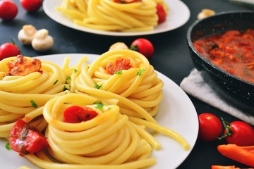 Pasta in a white plate on a dark background. Appetizing spaghetti with tomatoes and mushrooms. Top view food.