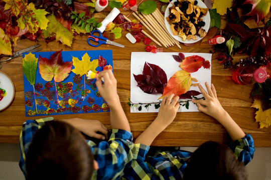 Children, applying leaves using glue, scissors, and paint, while doing arts and crafts in school.