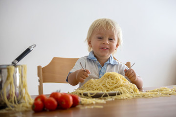 Little baby boy, toddler child, eating spaghetti for lunch and making a mess at home
