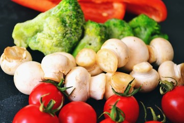 Fresh healthy vegetables. Vegetarian food. Sweet pepper, broccoli, cauliflower, mushrooms, tomato. Vegetables on a black dark background. Bright color food. Varied Food background. Place for text.
