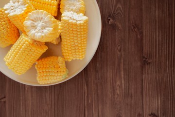 Sweet fresh corn on a beige ceramic plate on a wooden table. Top view, copy space for text.