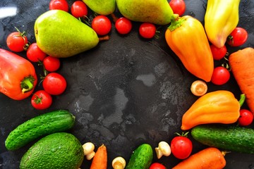 Composition with assorted fresh organic vegetables. Assorted fresh vegetables and fruits. Place for text. Cucumbers, tomatoes, pears, avocados, carrots, sweet peppers. Food on a dark table background.