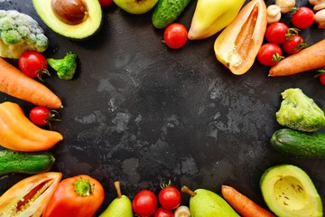 Composition with assorted fresh organic vegetables. Assorted fresh vegetables and fruits. Place for text. Cucumbers, tomatoes, pears, avocados, carrots, sweet peppers. Food on a dark table background.