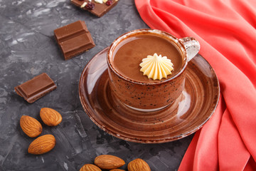 Cup of hot chocolate and pieces of milk chocolate with almonds on a black concrete background with red textile. side view.