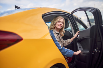 Photo of blonde sitting in back seat of yellow taxi with open door