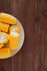 Sweet fresh corn on a beige ceramic plate on a wooden table. Top view, copy space for text.