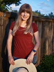 Outdoor lifestyle young happy beautiful blonde woman wearing trendy straw hat dressed red blouse blue jeans short emotionally posing in old street of european cozy village in evening warm autumn sun