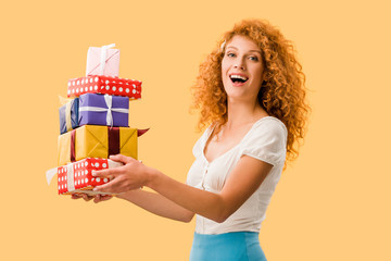 excited redhead girl holding presents isolated on yellow