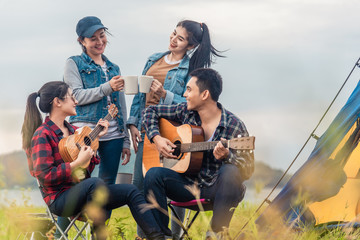 Group of Asian friends having fun eating barbecue outdoor while camping and play guitar.
