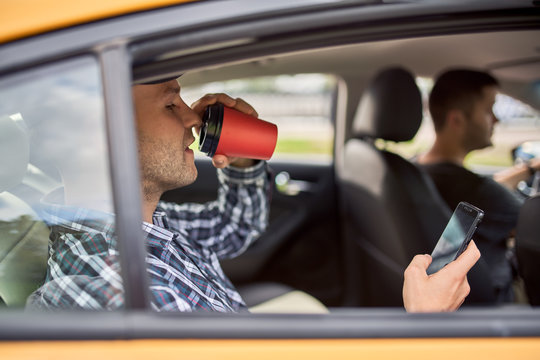 Picture of man with phone and glass of coffee sitting in back seat in taxi