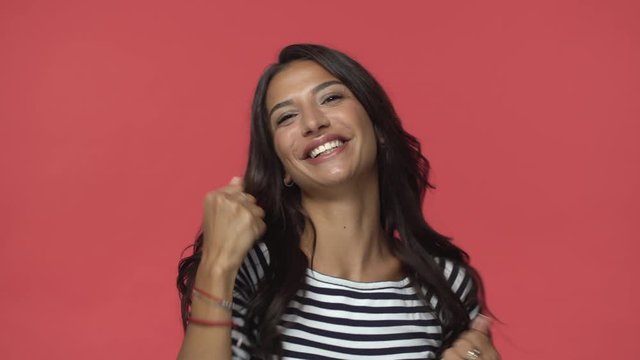 Happy indian woman gasping upbeat fist pumping, raise hands up in triumph and joy, looking surprised and enthusiastic as hear she won big prize, celebrating awesome news, stand red background