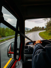 Image from passenger compartment of car driving along road among green trees in Norway on summer.