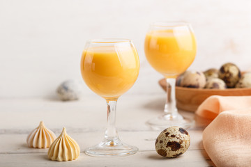 Sweet egg liqueur in glass with quail eggs and meringues on white wooden background. Side view, close up. - obrazy, fototapety, plakaty