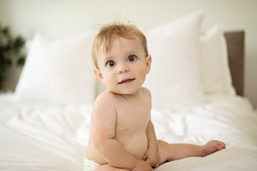 Cute happy baby girl in diaper on bed