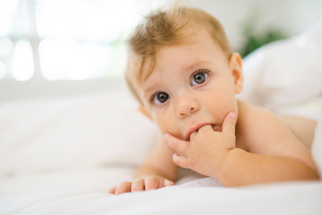 small baby boy sucking his finger on the white bedroom