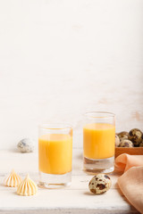 Sweet egg liqueur in glass with quail eggs and meringues on white wooden background. Side view, copy space, vertical.