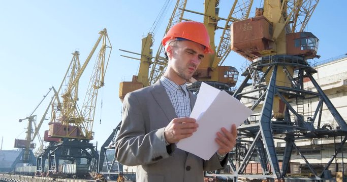 Young male worker of sea harbor in helmet, cargo manager in suit and halmet works outdoor , cranes and sea background	