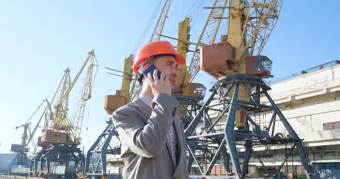 Young male worker of sea harbor in helmet, cargo manager in suit and halmet works outdoor , cranes and sea background	