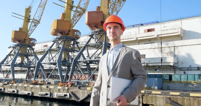 Young male worker of sea harbor in helmet, cargo manager in suit and halmet works outdoor , cranes and sea background	