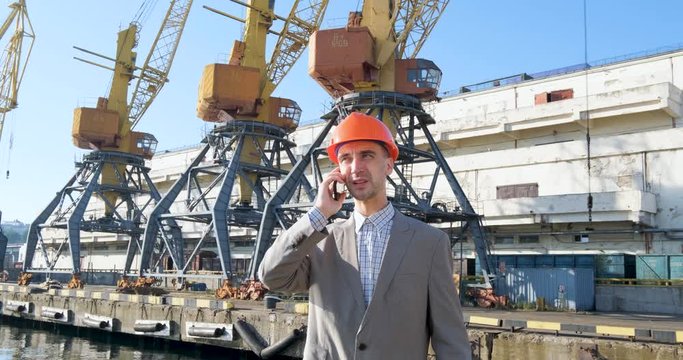 Young male worker of sea harbor in helmet, cargo manager in suit and halmet works outdoor , cranes and sea background	