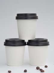 Pyramid made from white paper cups with coffee beans isolated on white. Mockup with copyspace