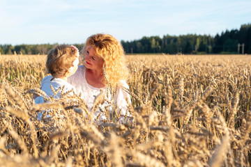 A girl with red hair hugs a little girl, daughter. The family is sitting on the field with ripe ears of corn. Woman and child in white shirts. look at the sunset and rejoice. Countryside and sunset.