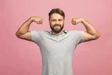 Waist-up portrait of muscular young man flexing his biceps against pink background.
