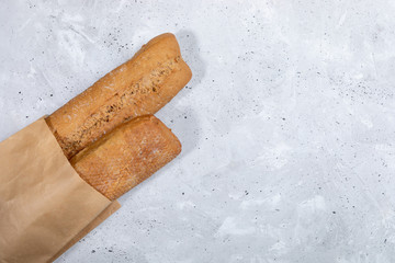 Fresh baked bread baguettes in paper bag on grey concrete background with copy space.