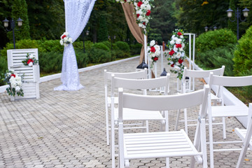 Outdoor wedding decorations, arch decorated with red and white flowers, chairs, lanterns.
