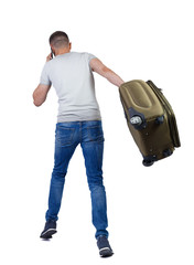 Back view of walking man with suitcase talking on the smartphone.