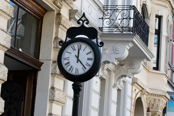 Fototapeta na wymiar A round metal clock on a post on the street that shows twelve hours and twenty-three minutes