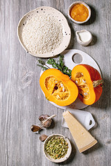 Ingredients for cooking pumpkin risotto. Raw uncooked risotto rice in ceramic bowl, sliced pumpkin, cream, seeds, parmesan cheese, garlic and herbs over grey wooden background. Flat lay, space