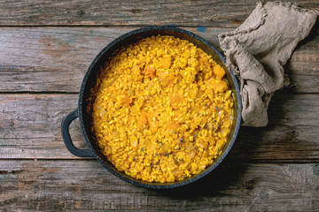 Traditional vegetarian pumpkin risotto italian dish in iron pan with cloth rag over old wooden background above. Flat lay, space