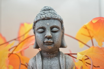 A Buddha statue with a stunning Japanese maple leaf background.
